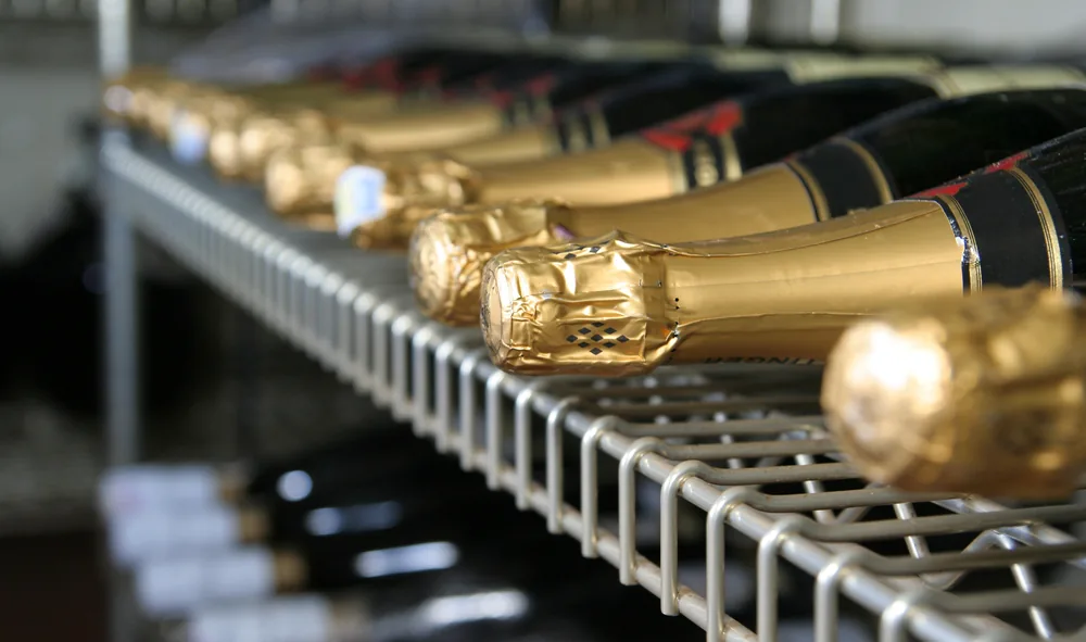 Gold-capped Champagne bottles lying in a row on a wire shop shelf