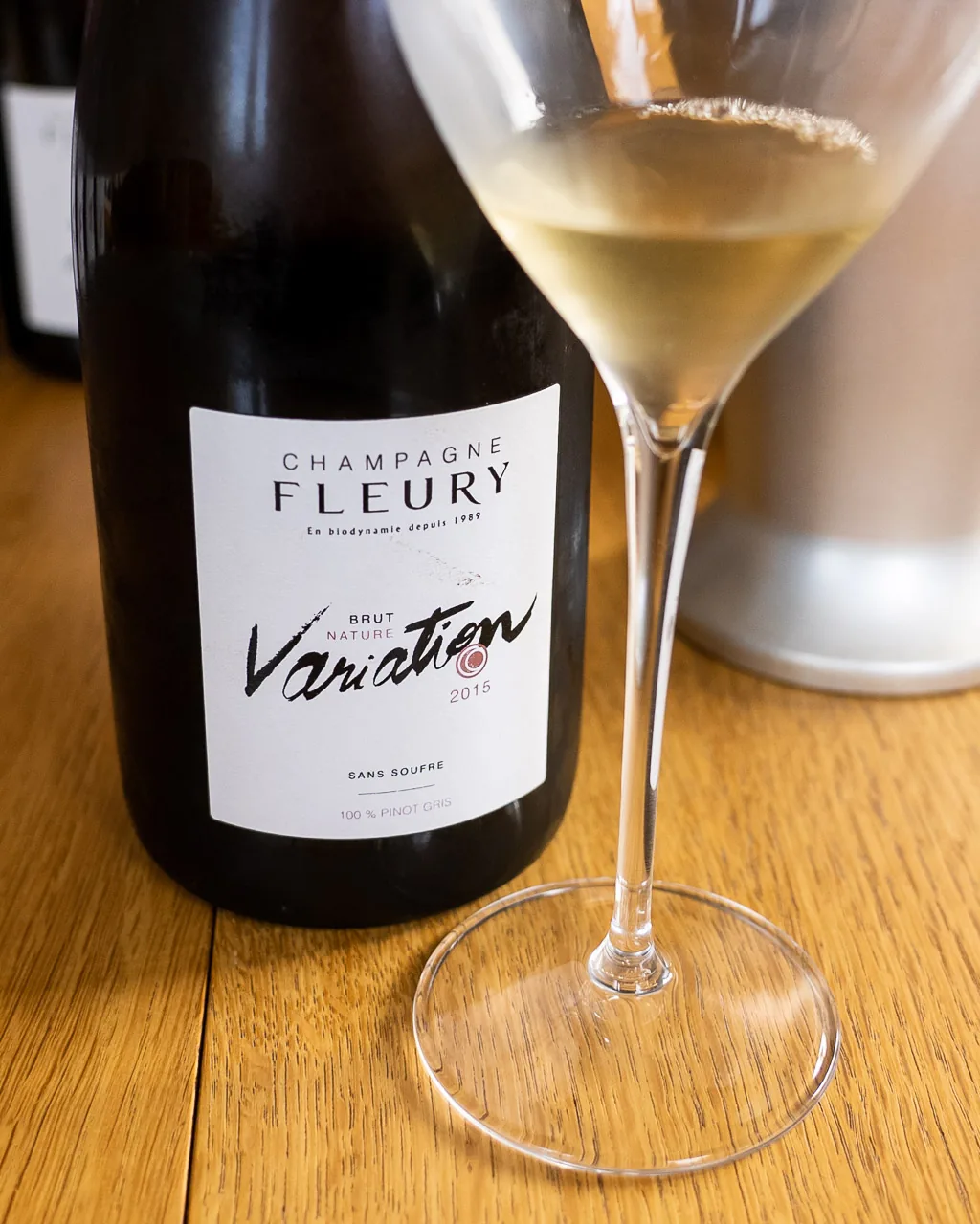 A bottle of Champagne Fleury Variation Brut Nature beside a filled glass on a wooden table