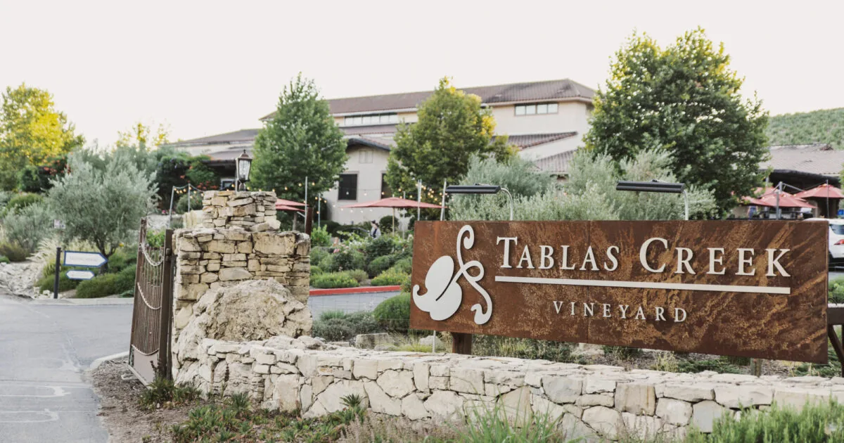 The weathered corten-steel Tablas Creek Vineyard entrance sign set on a dry-stone wall, with the winery and gardens behind