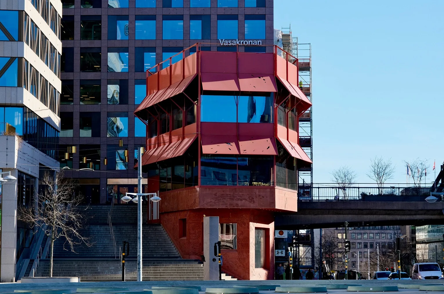 Röda Huset in Stockholm: the red steel-and-glass pavilion on its plaza, awnings angled out over two floors of windows, a tower block rising behind it