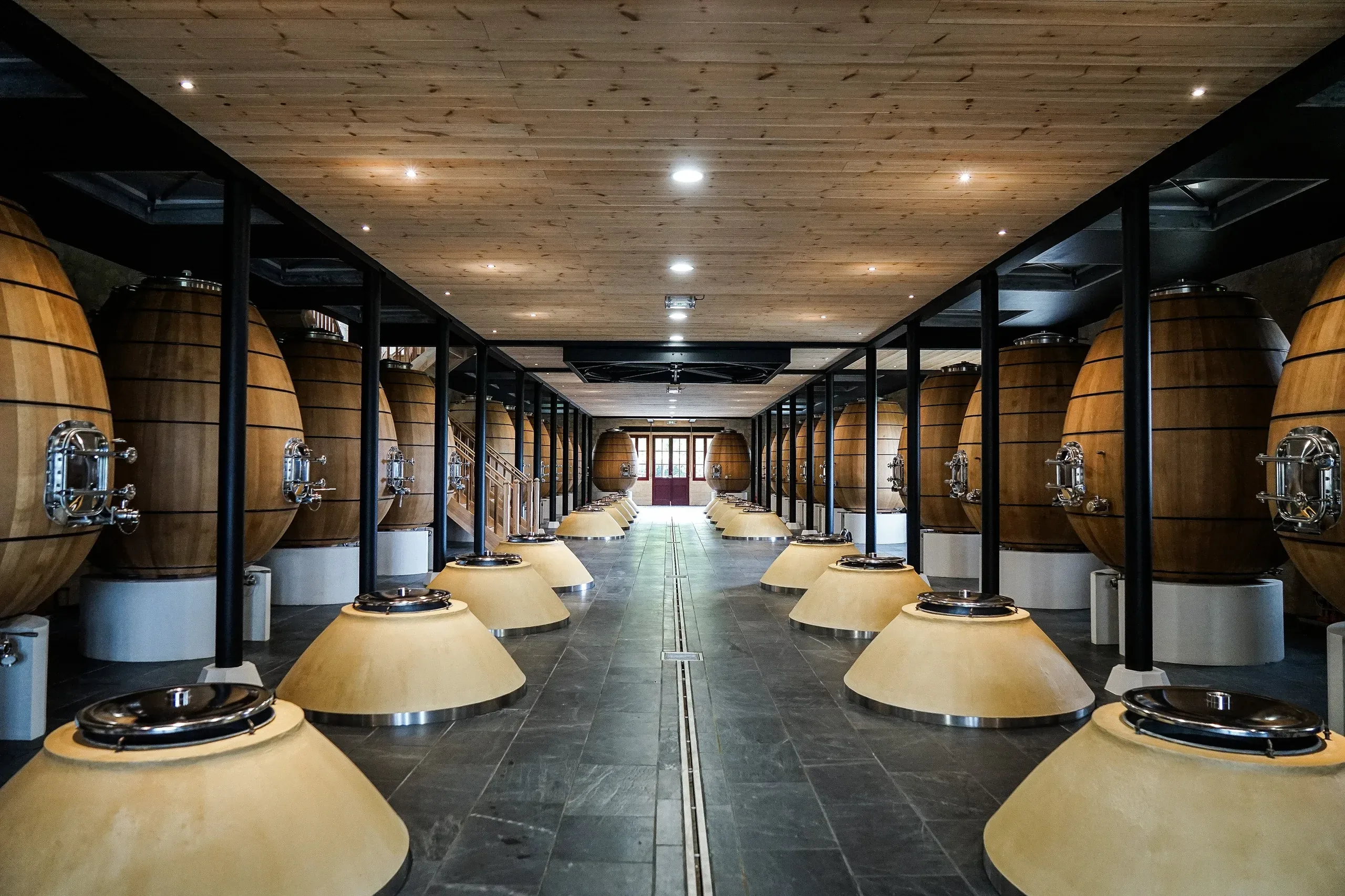Rows of tall clay amphorae under a timber ceiling in the Pontet-Canet cellar