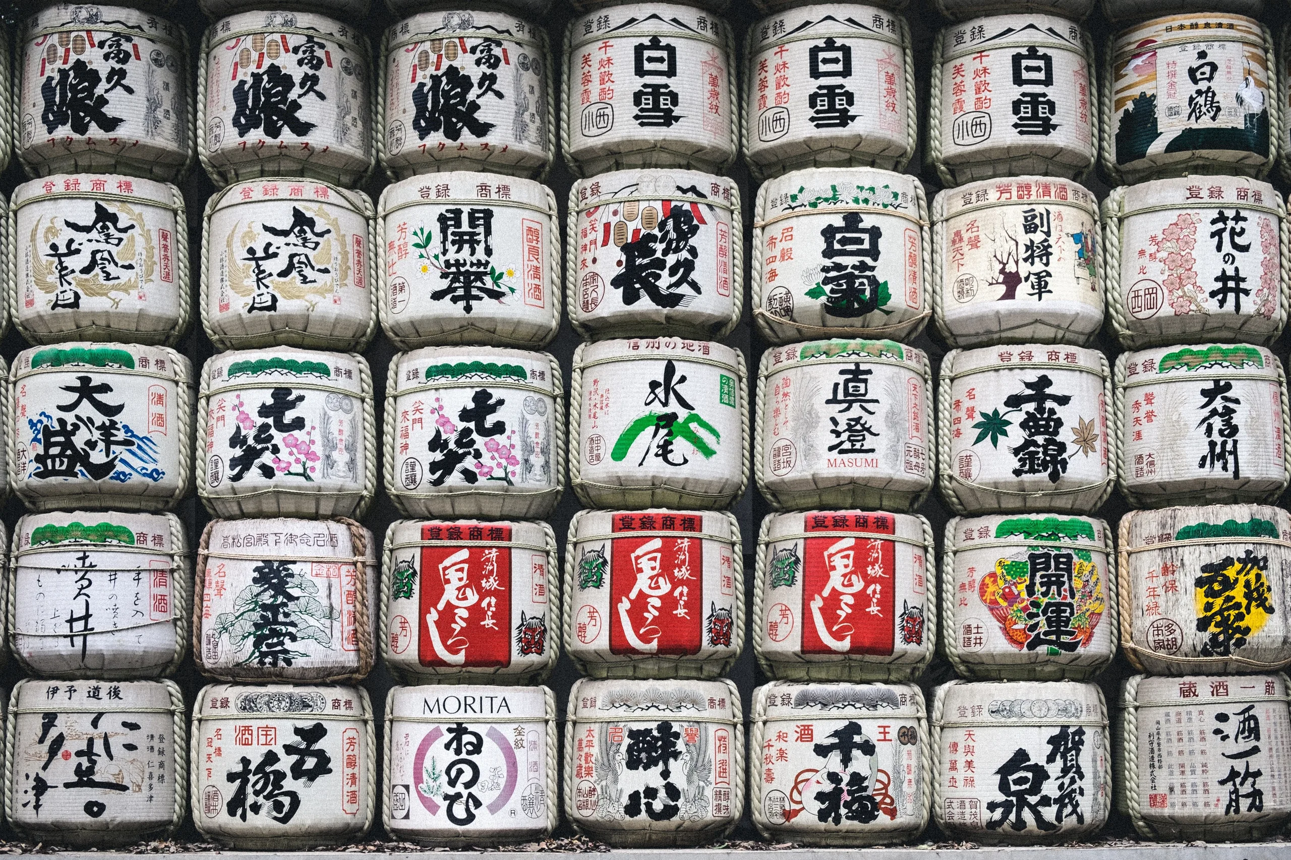 A wall of straw-wrapped kazaridaru sake barrels painted with brewery marks