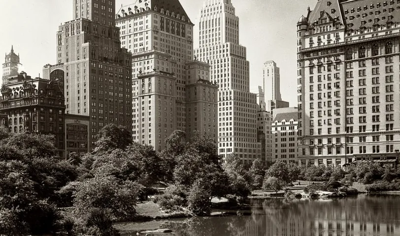 A sepia photograph of skyscrapers above trees, reflected in a pond