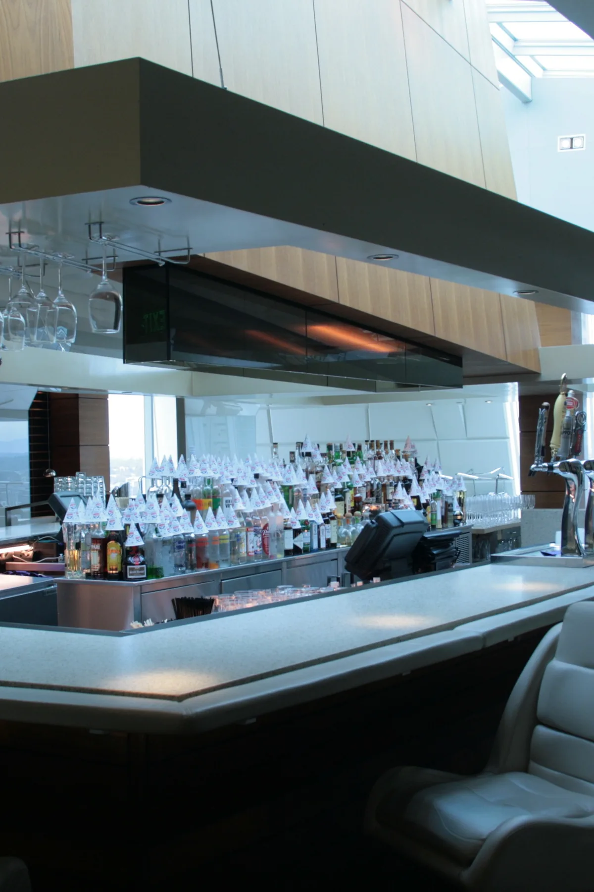 An island bar with a white leather stool, hanging wine glasses and a back bar of spirits bottles in daylight