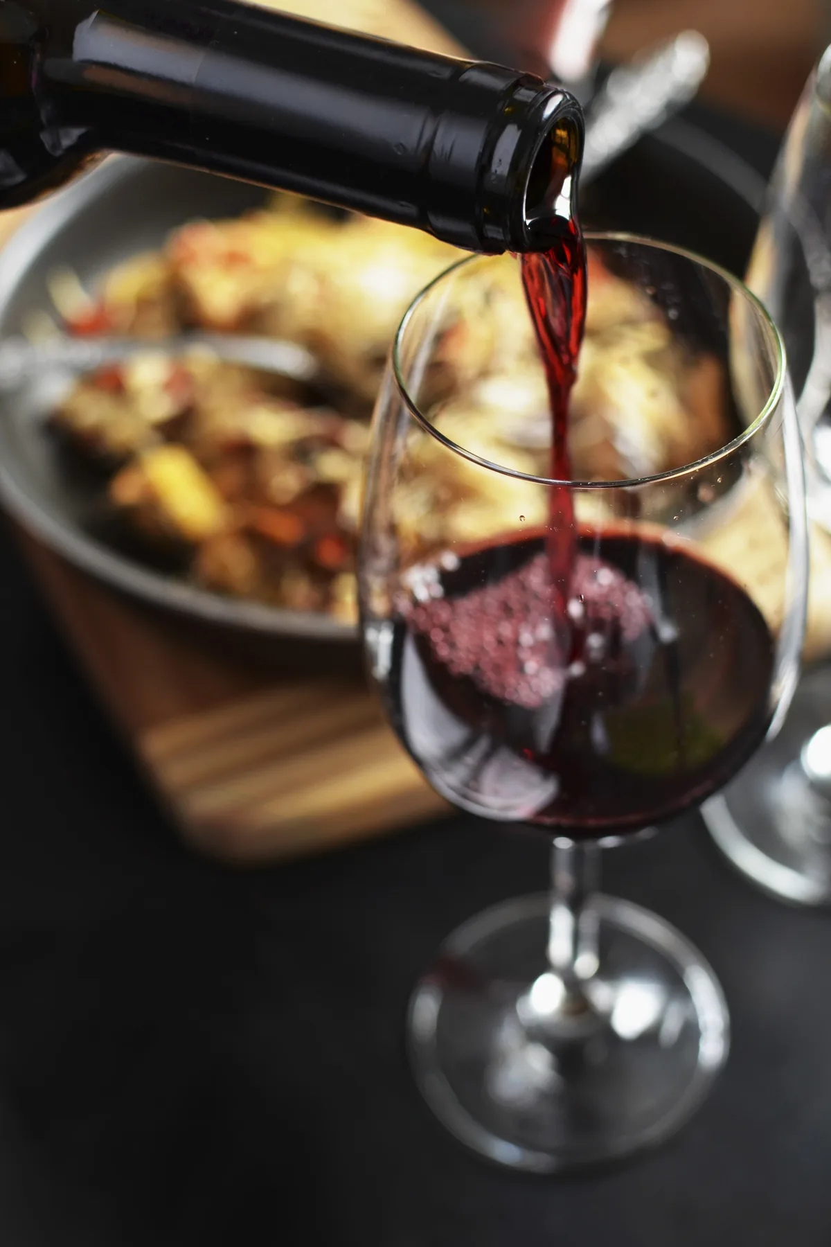 Red wine pouring into a glass beside a plate of food