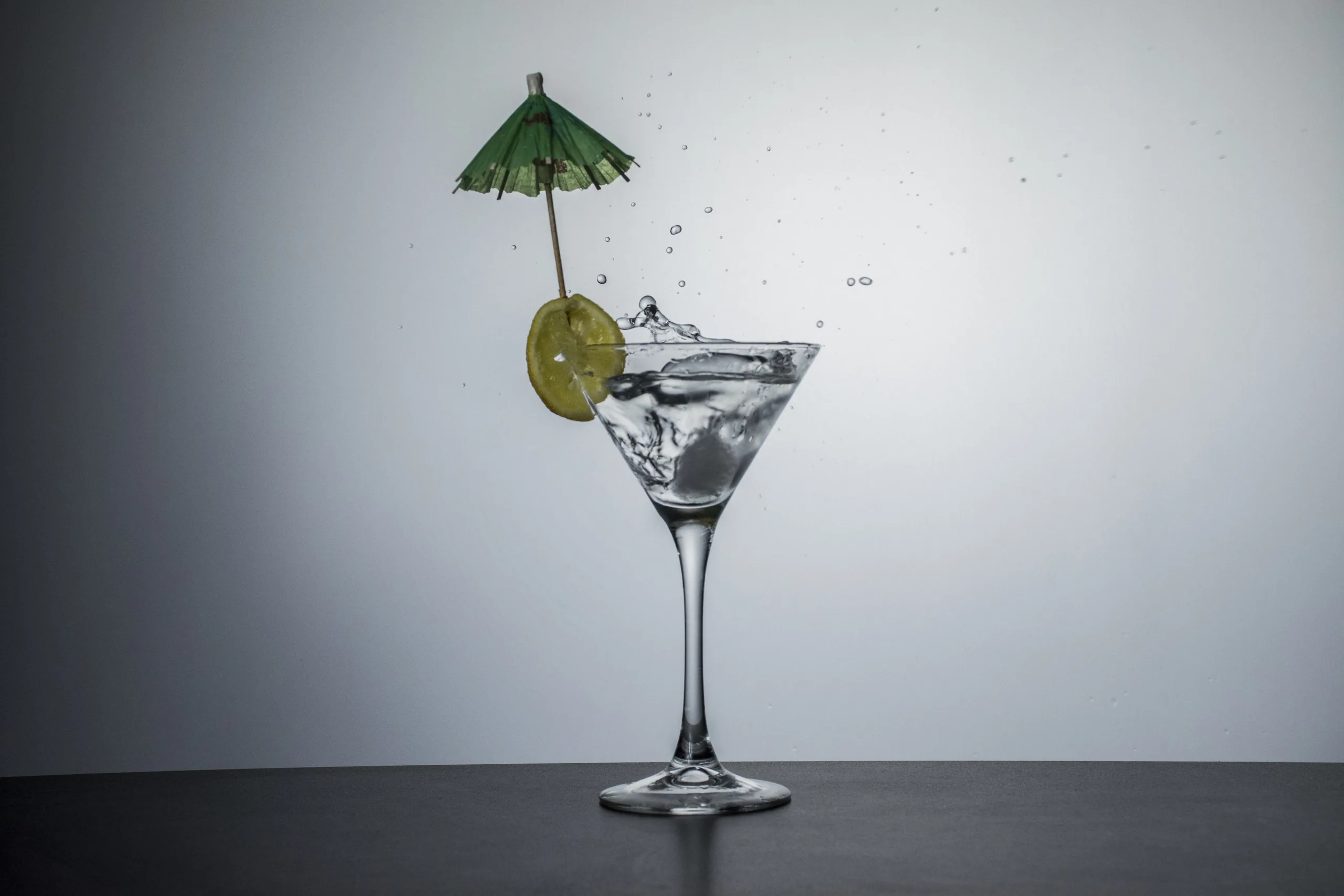 A martini glass of clear spirit with a lime slice and a small paper parasol