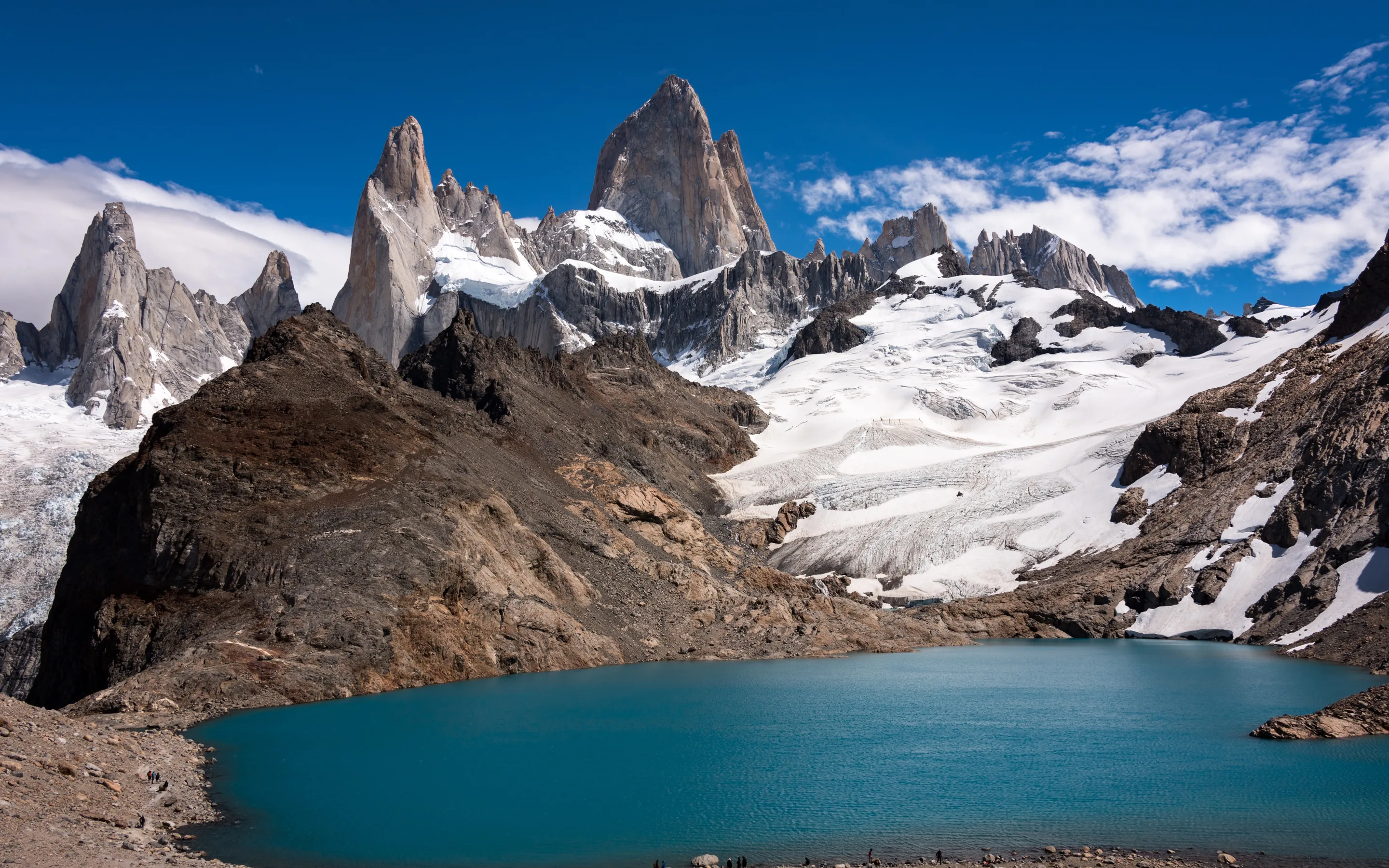 The granite spires of Monte Fitz Roy, on the border between Chile and Argentina in Patagonia, above a glacier and a turquoise lake under a deep blue sky.