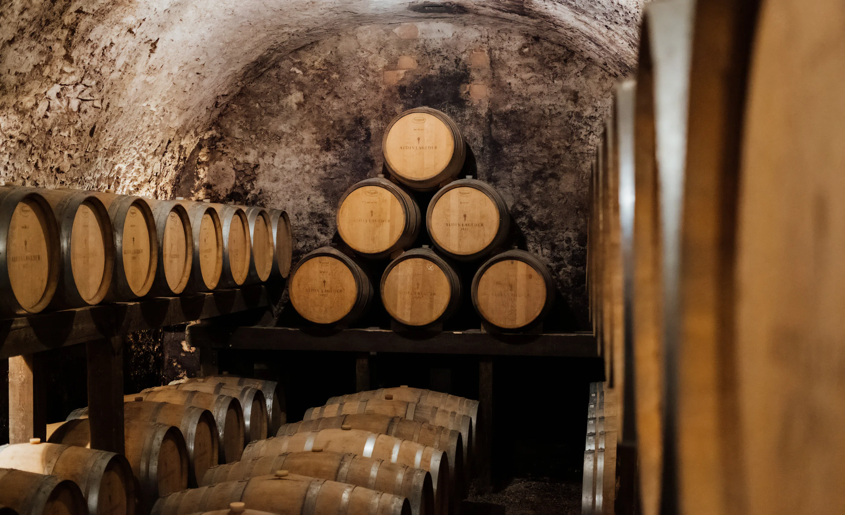 Vaulted stone cellar with oak barrels stacked in a pyramid, the barrel heads branded Alois Lageder