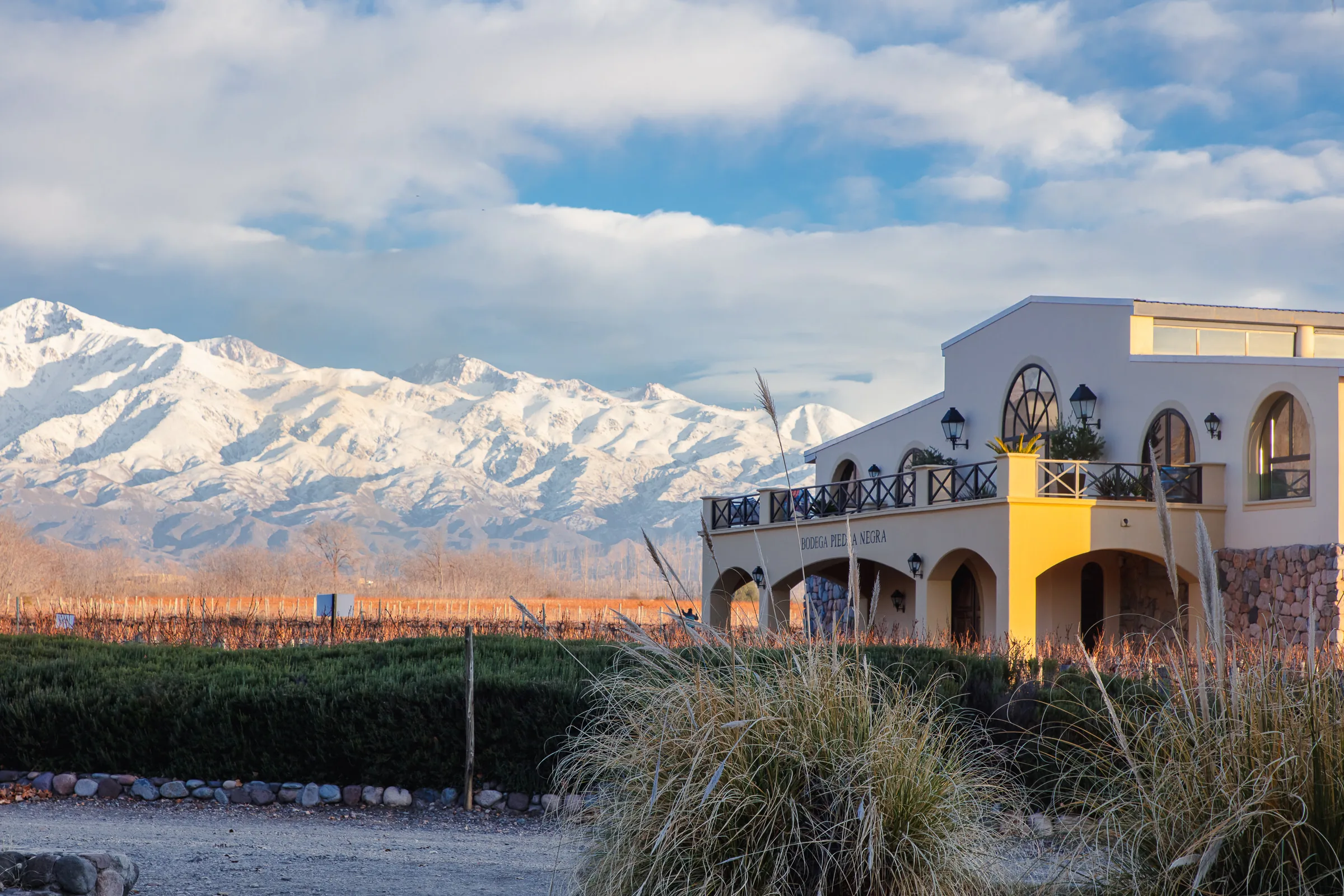 Cream building with arched windows and a balcony, signed Bodega Piedra Negra, below a snow-covered mountain range