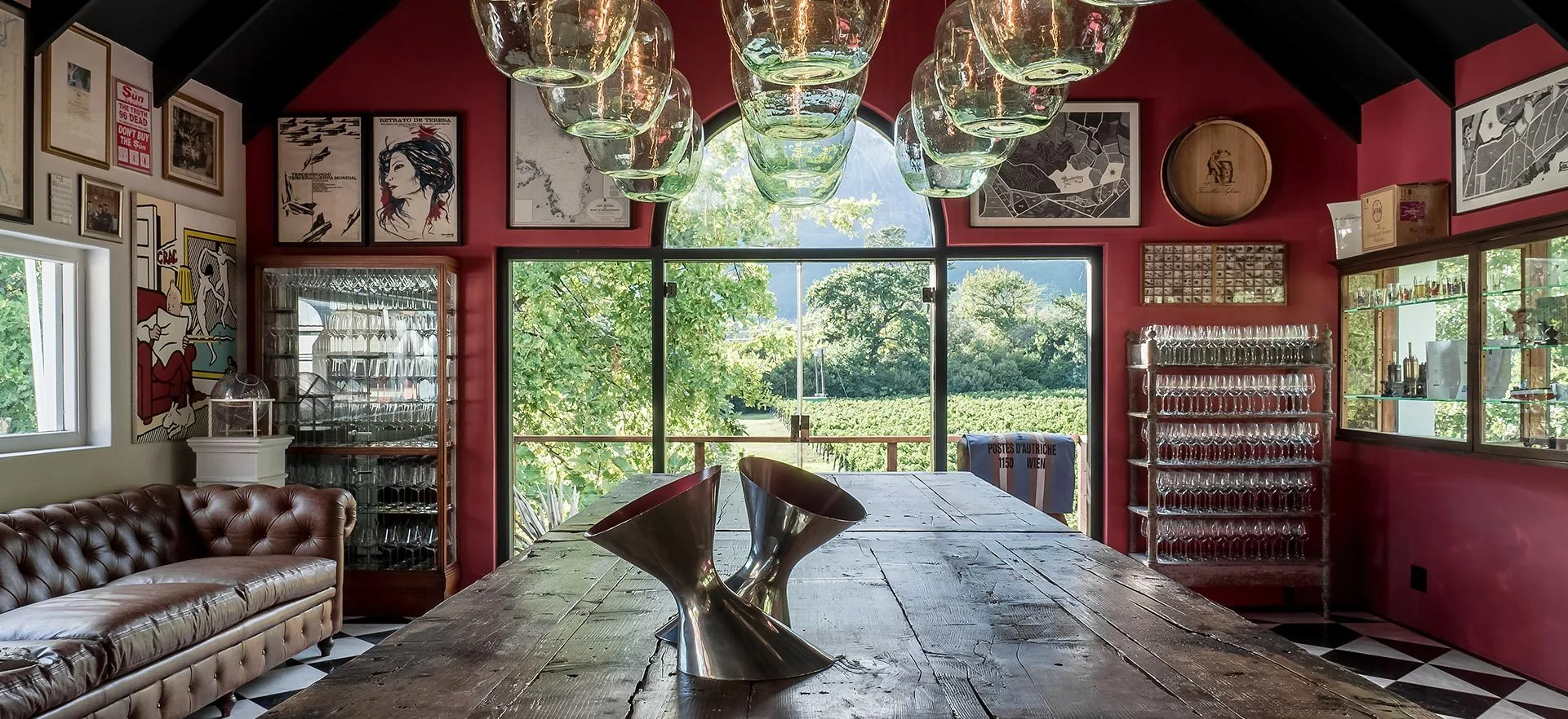 Red-walled tasting room at Boekenhoutskloof with a long wooden table, glass pendant lamps and an arched window onto vines