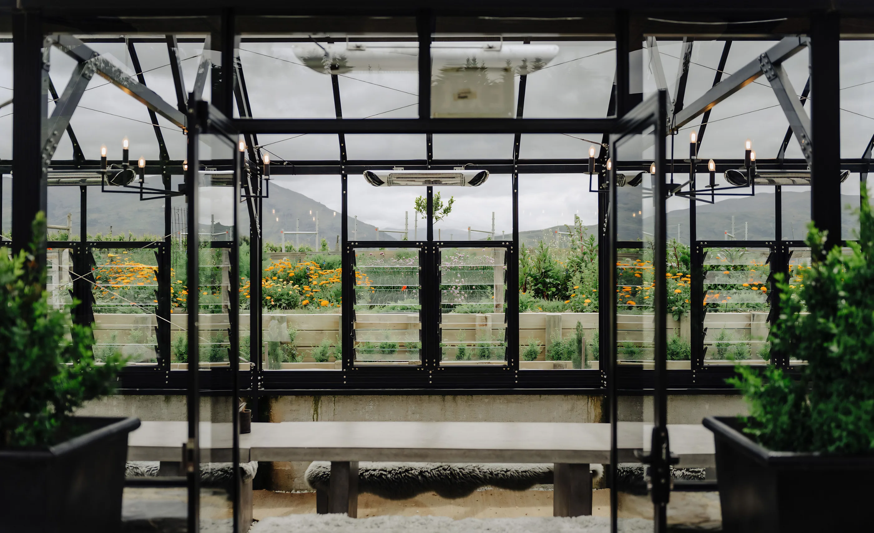 Glass-walled dining room at Carrick Winery with candle sconces, looking out to a flower garden and mountains