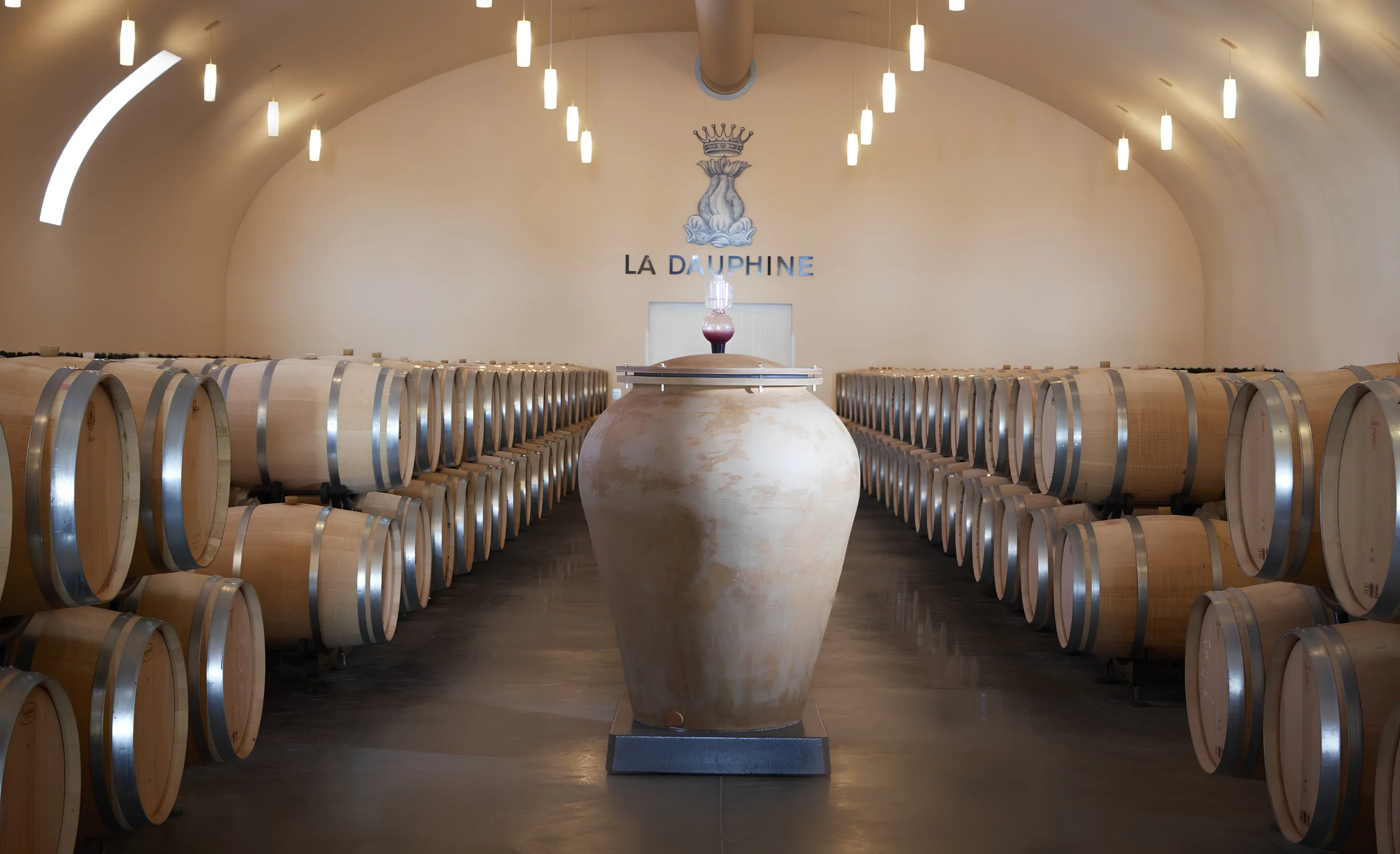 Barrel hall with a large terracotta-coloured jar between rows of oak barrels beneath a wall sign reading La Dauphine