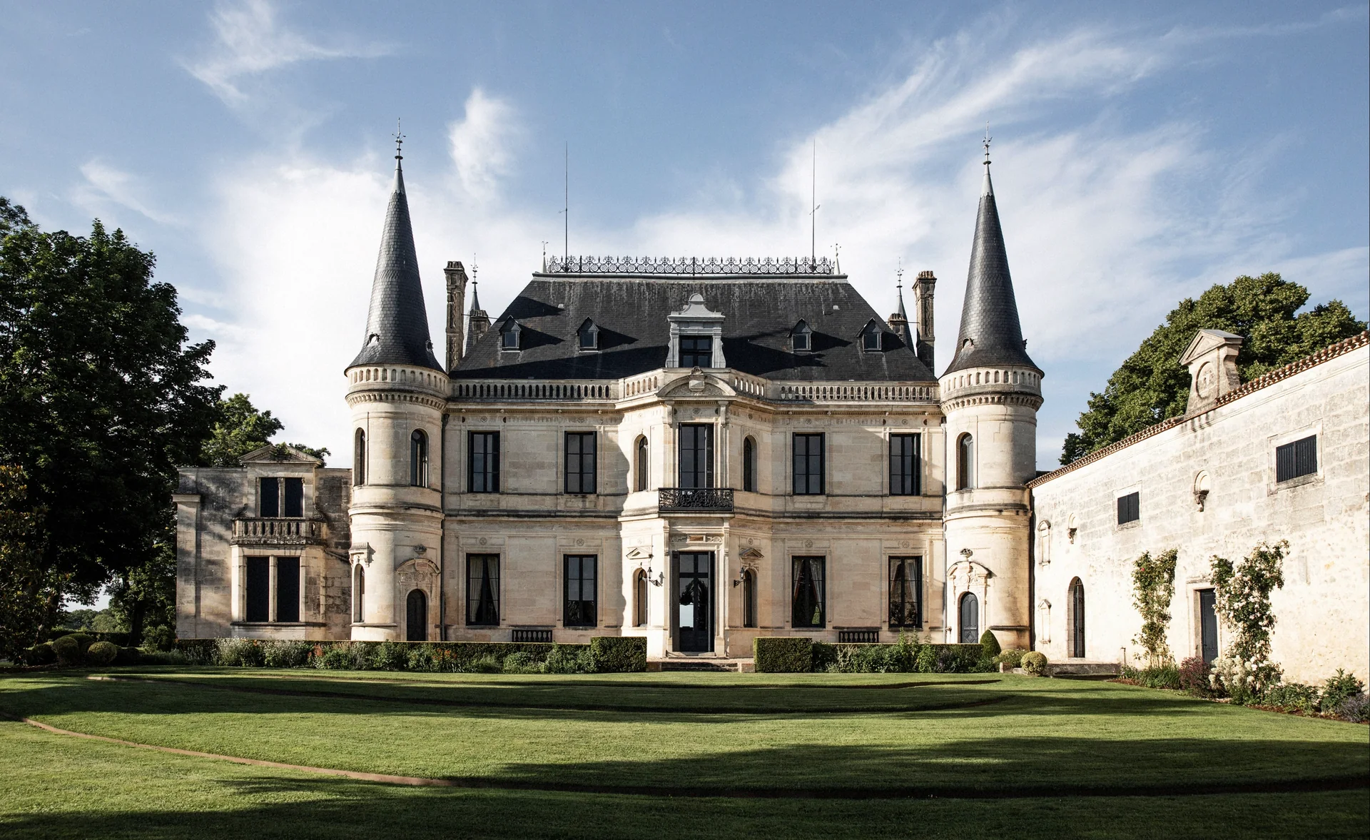 Stone château with two pointed slate-roofed towers and a mansard roof, seen across a trimmed lawn