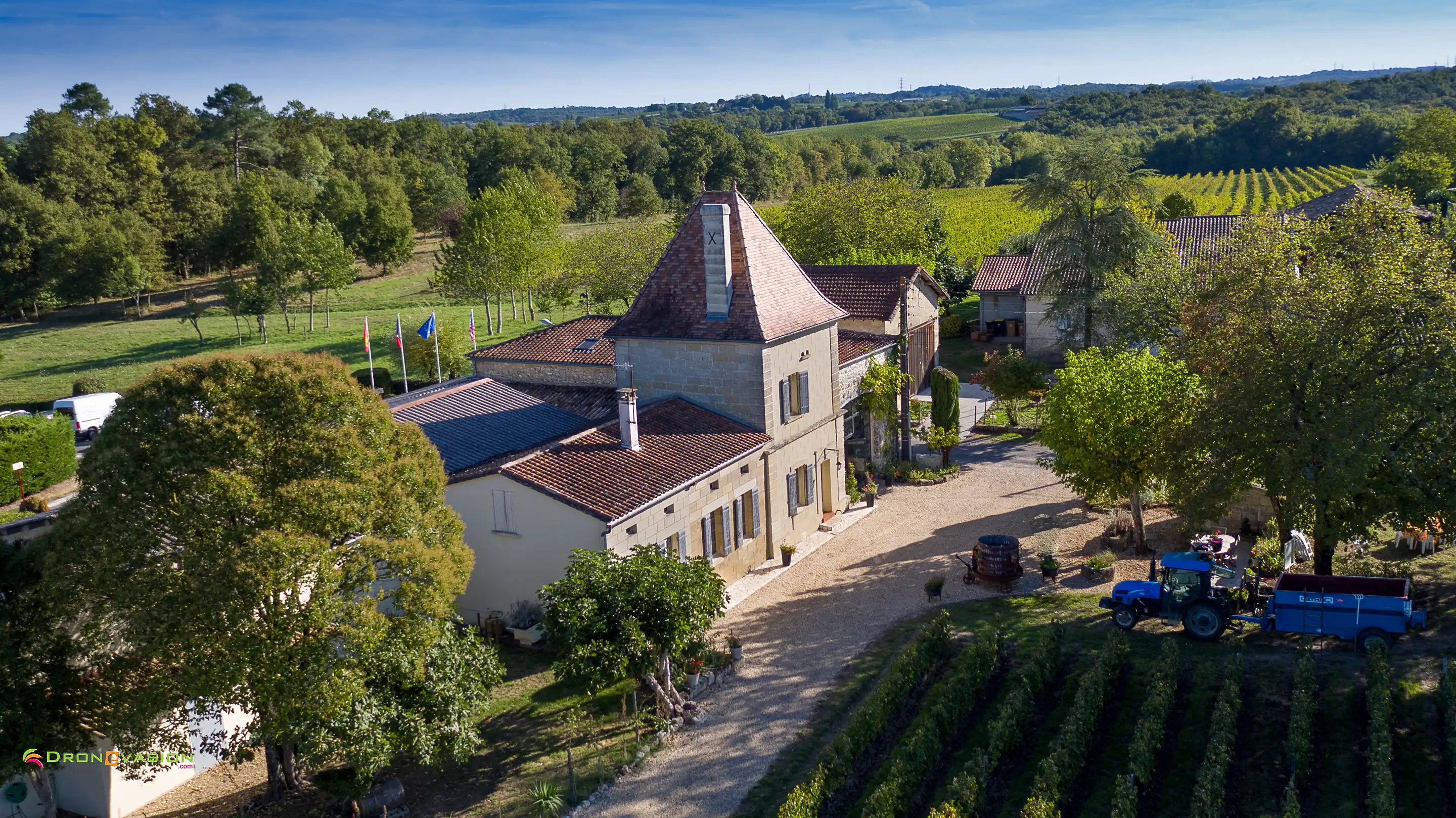 Aerial view of a tile-roofed château, courtyard and blue tractor, vines in front and woods behind, at Château Vieux Mougnac