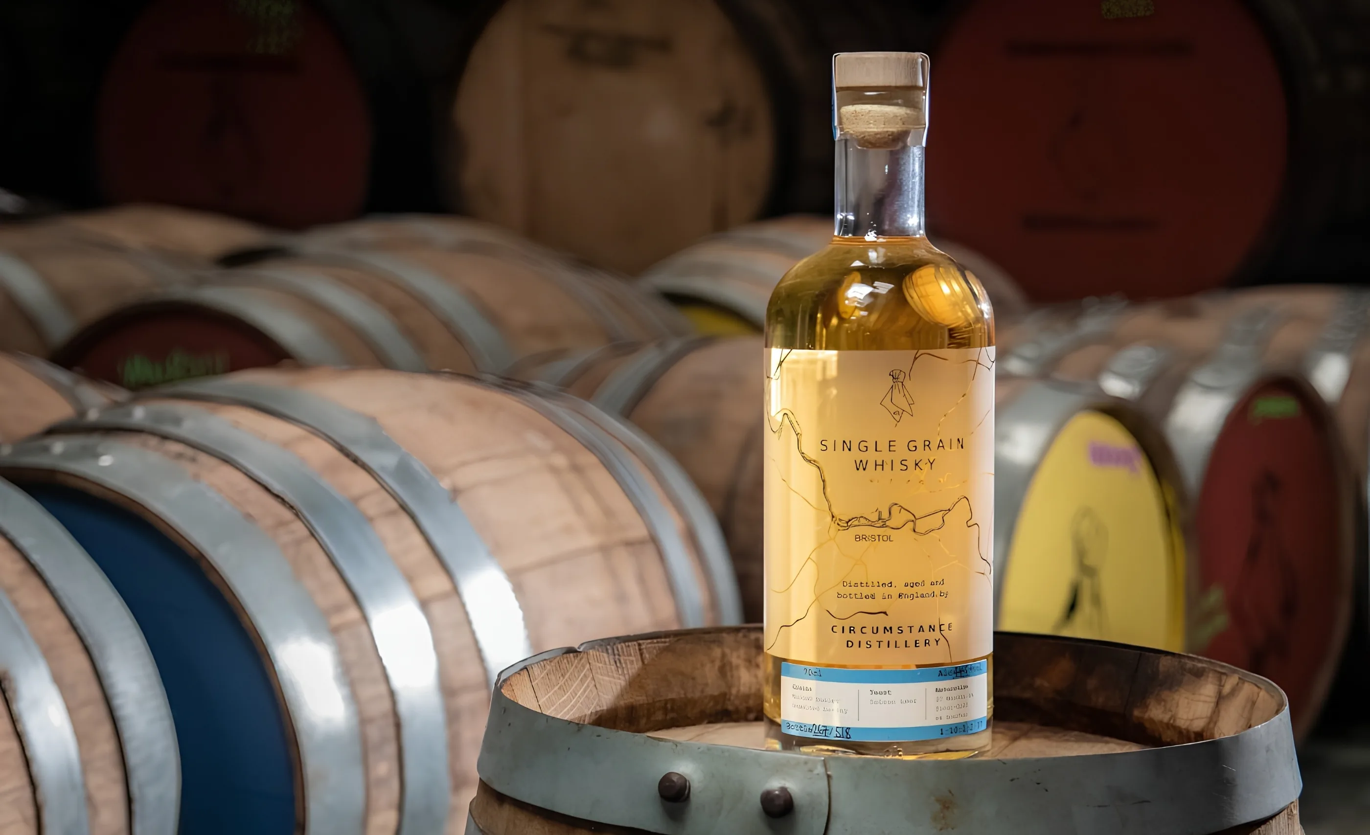 Bottle of Circumstance Distillery single grain whisky standing on a cask top before rows of barrels with painted ends