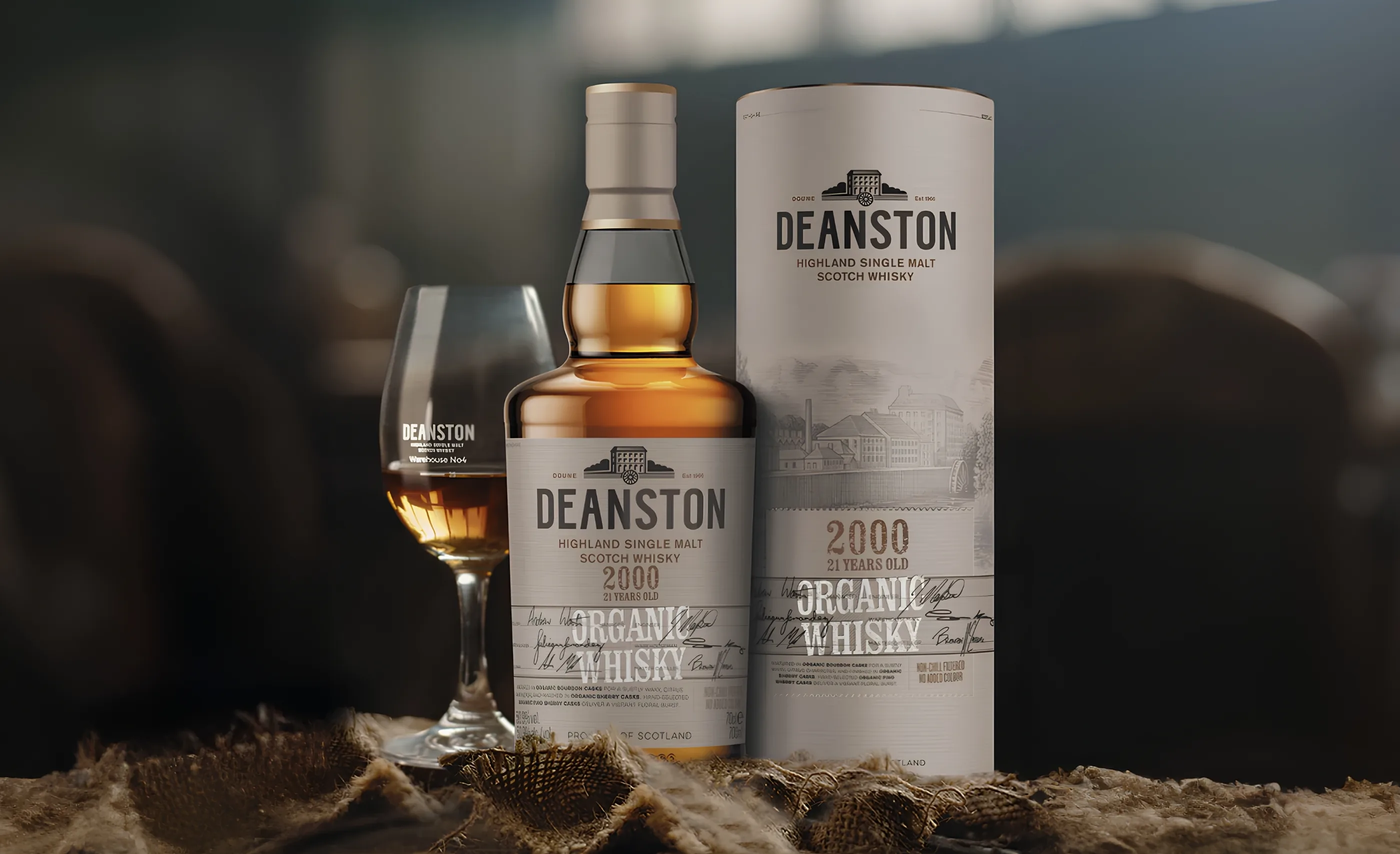 A bottle of Deanston Highland Single Malt Scotch Whisky, 21 years old, with its tube and a glass of whisky on hessian
