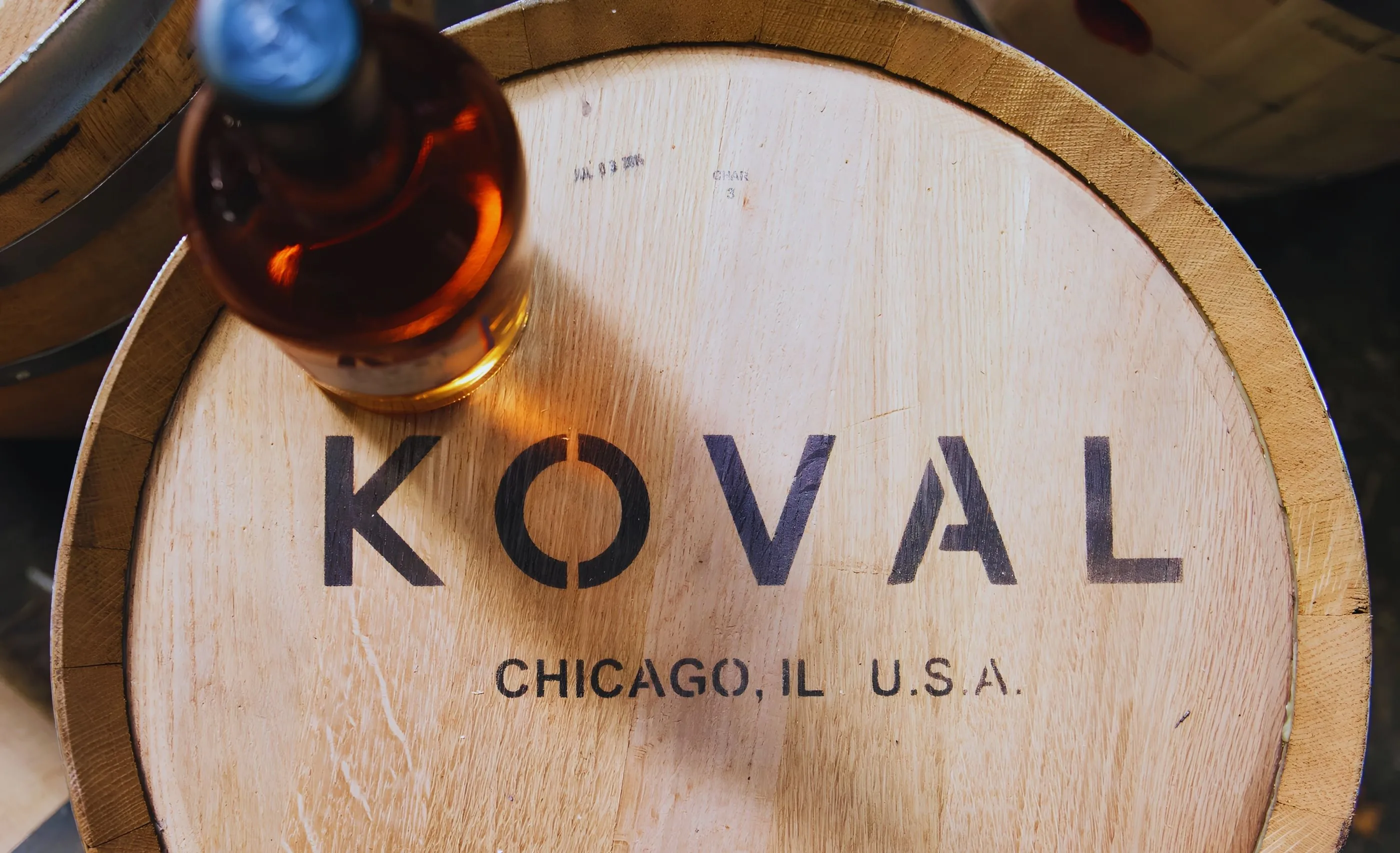 A barrel head stencilled Koval, Chicago, IL, U.S.A., with a bottle of amber spirit resting on it