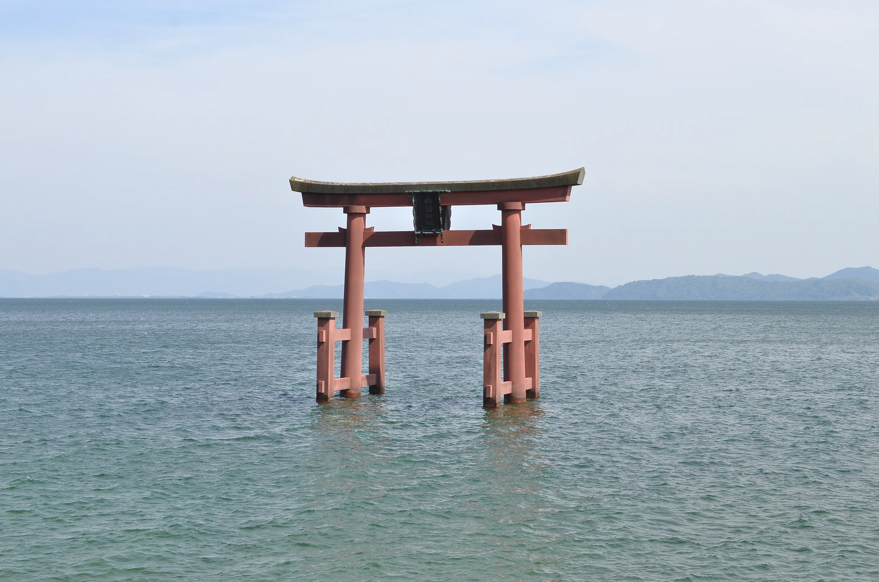 The red torii of Shirahige Shrine standing in the water of Lake Biwa, Shiga, with hazy mountains on the far shore