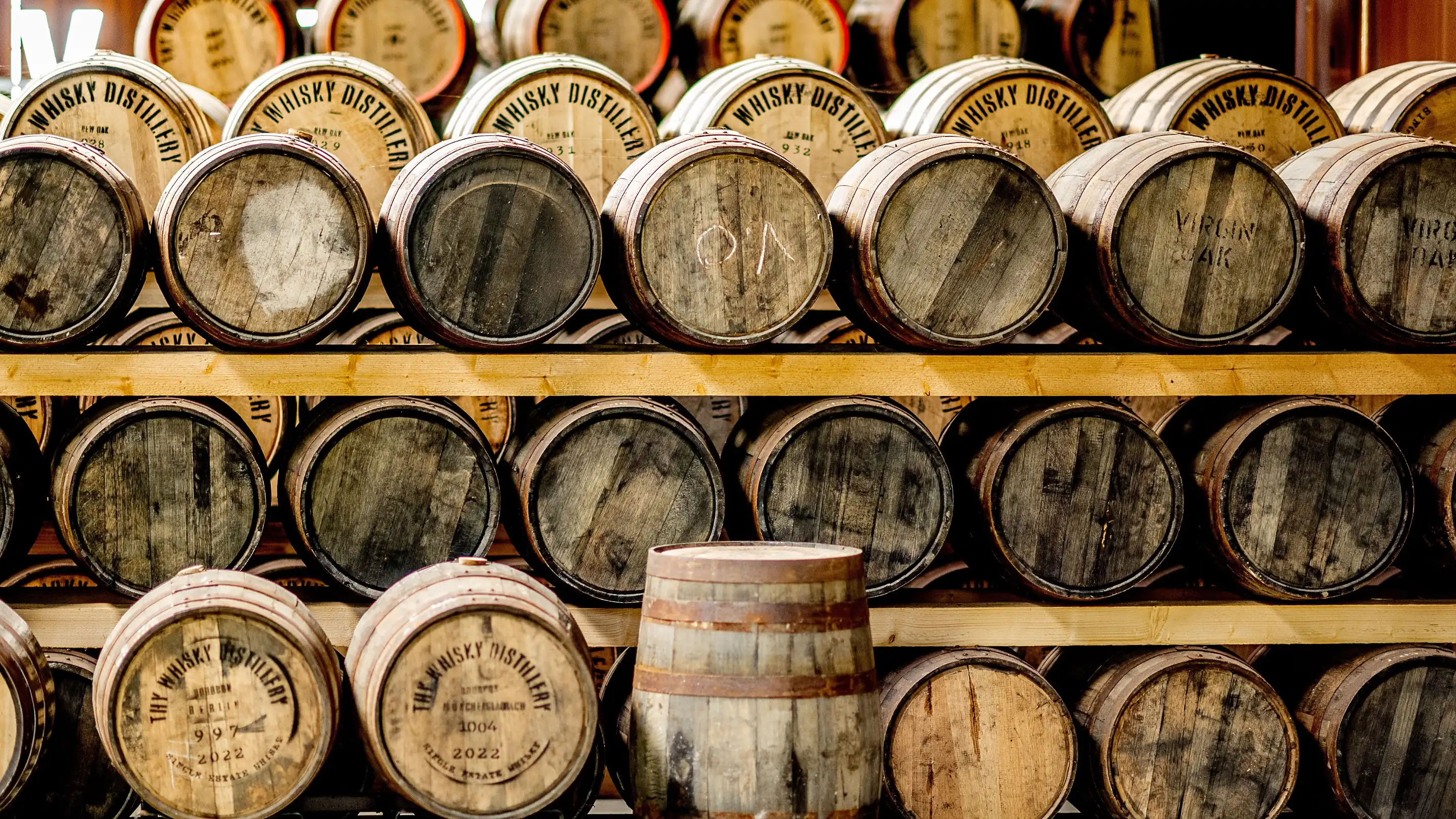 Barrels stacked on wooden racks, their ends stencilled Whisky Distillery, one marked Virgin Oak