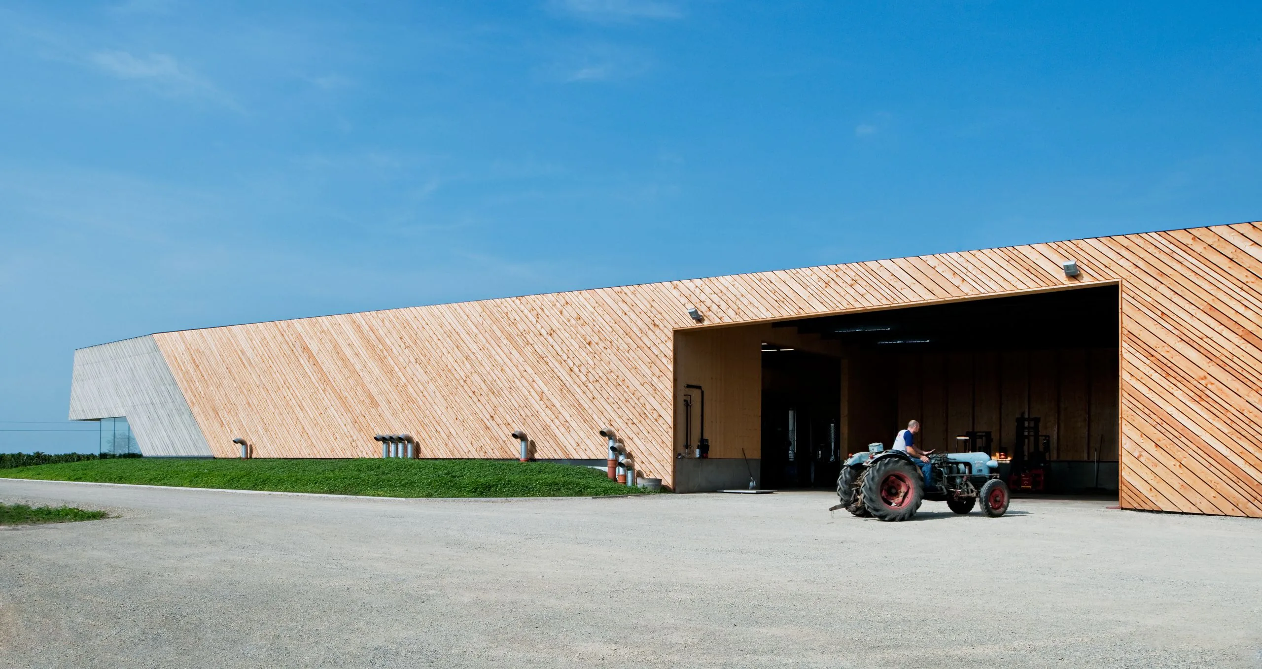 Long timber-clad cellar building at Weingut Claus Preisinger, with an old blue tractor in front of its open bay
